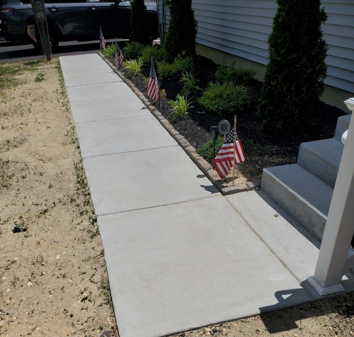 New concrete walkway and front steps alongside a freshly mulched garden bed