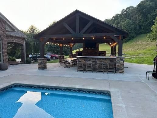 Covered outdoor pavilion with an outdoor kitchen and bar next to a concrete pool deck