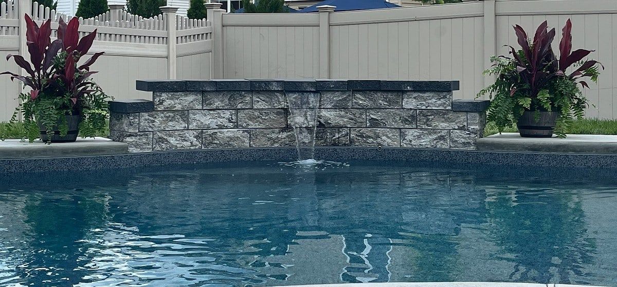 Stone veneer waterfall wall spilling into a backyard pool, framed by tropical planters