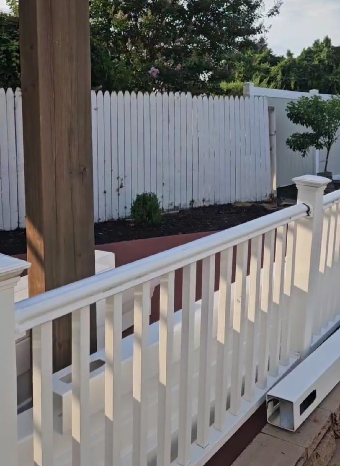 White vinyl railing and cedar pergola post overlooking a freshly mulched backyard